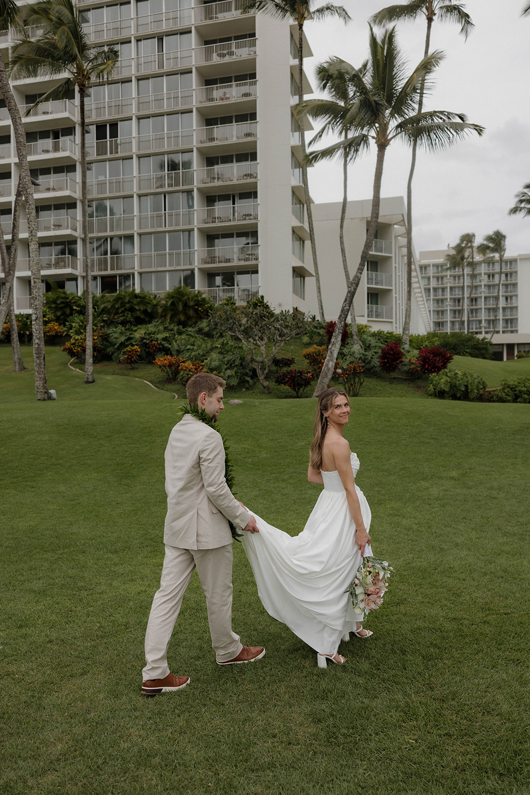 Close-up of the couple smiling at the camera while holding a pastel tropical bouquet by the ocean.