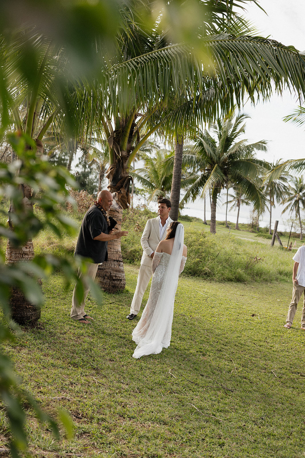 Officiant speaking with bride and groom during Maui elopement ceremony under palm trees

