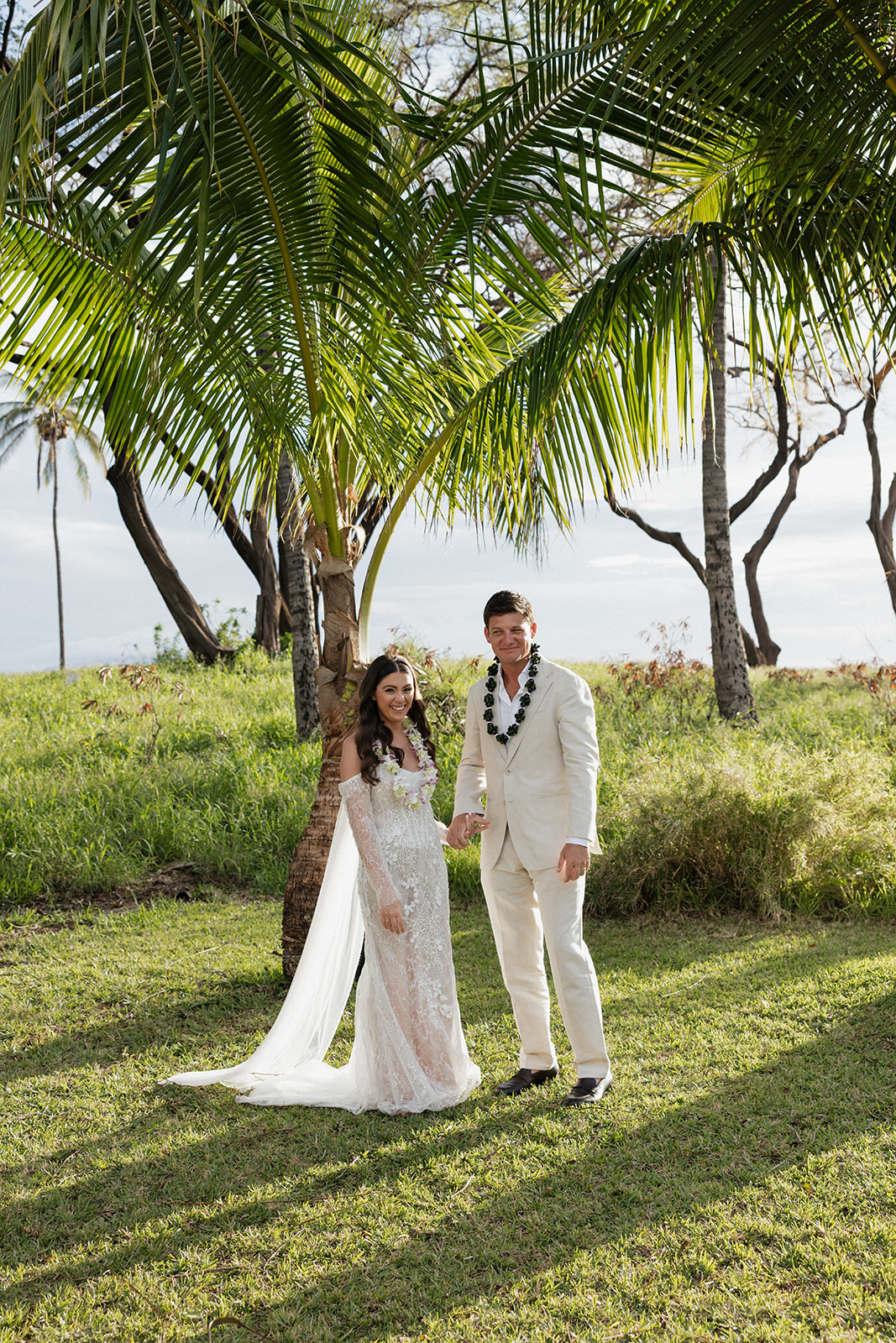 Bride and groom holding hands and smiling after their Maui elopement under a palm tree
