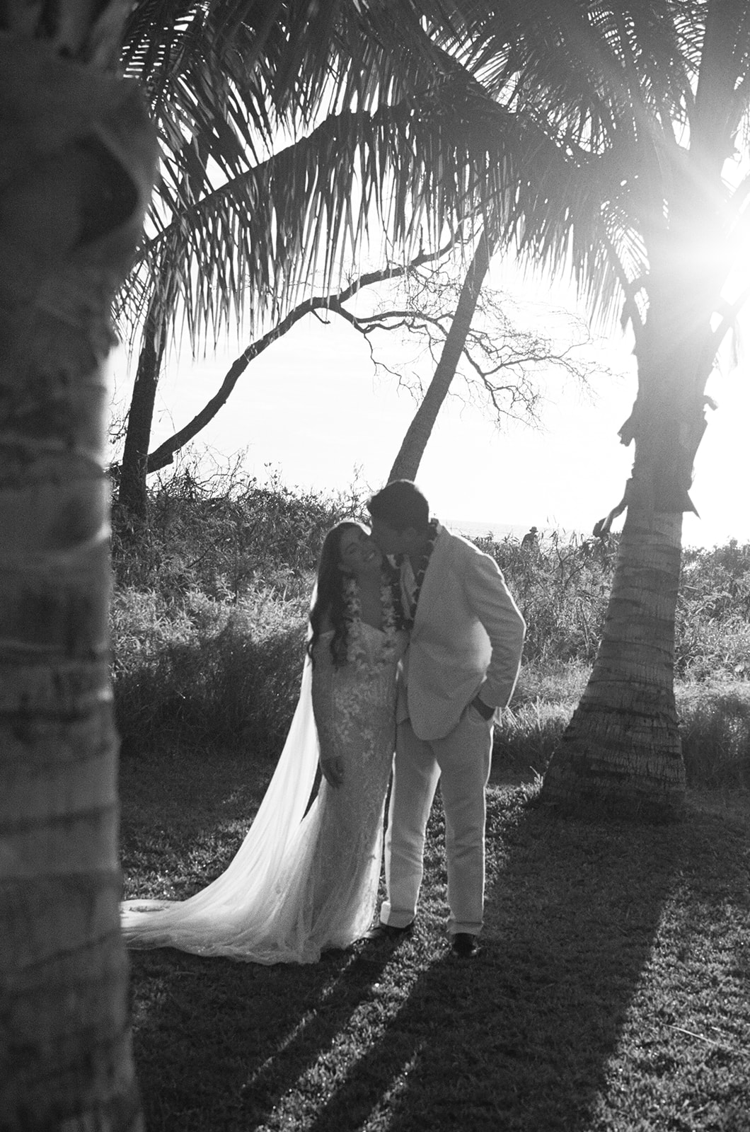 Black and white silhouette of bride and groom embracing between palm trees at a Hawaii wedding
