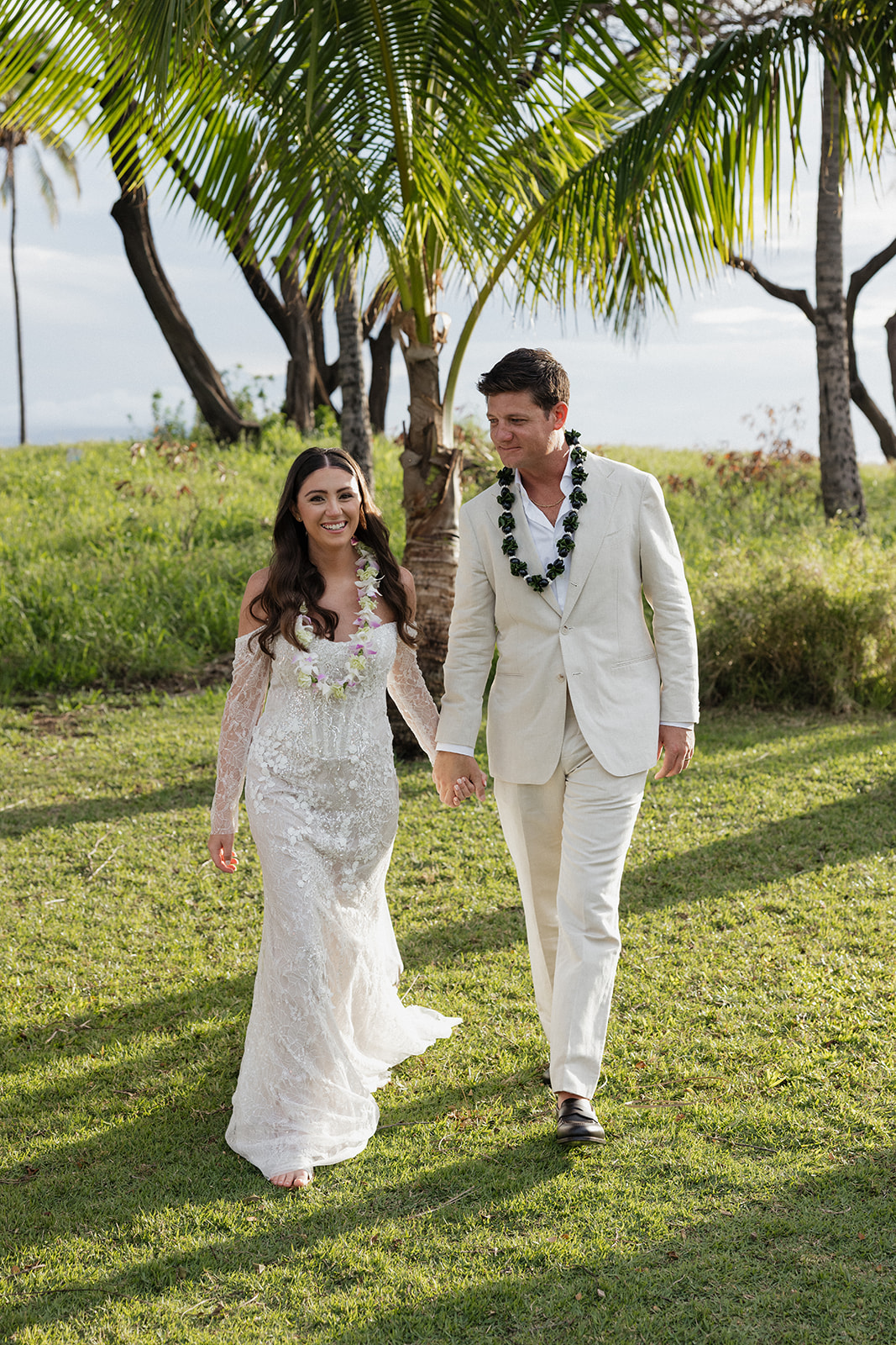 Bride and groom wearing leis and walking together through a grassy field during their Maui elopement

