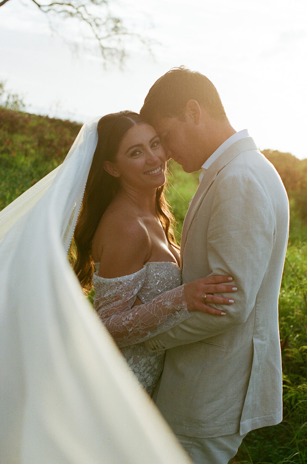 Bride smiling over her shoulder while embracing groom during their Maui elopement at golden hour
