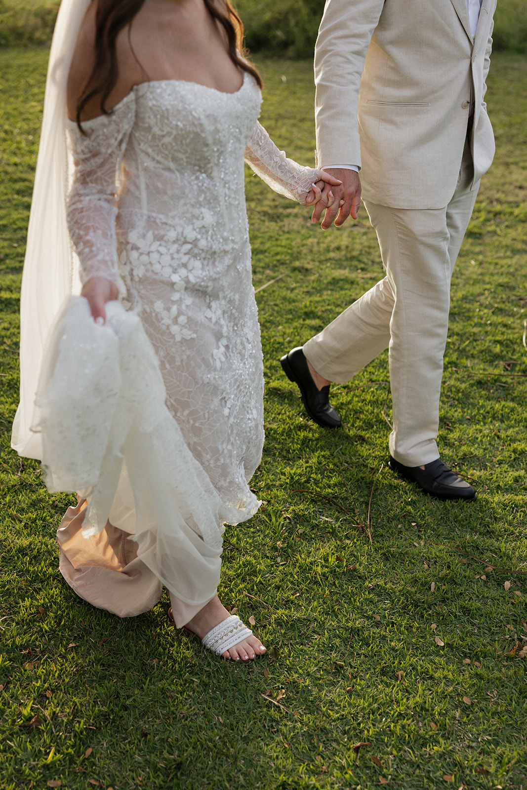 Close-up of bride and groom holding hands while walking across the grass at their Hawaii wedding
