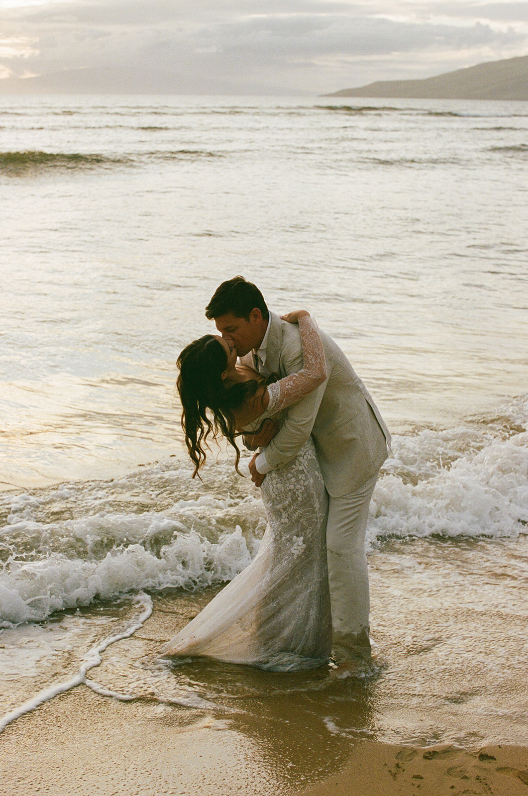 Groom dipping bride for a kiss while standing in the ocean waves during their Maui elopement
