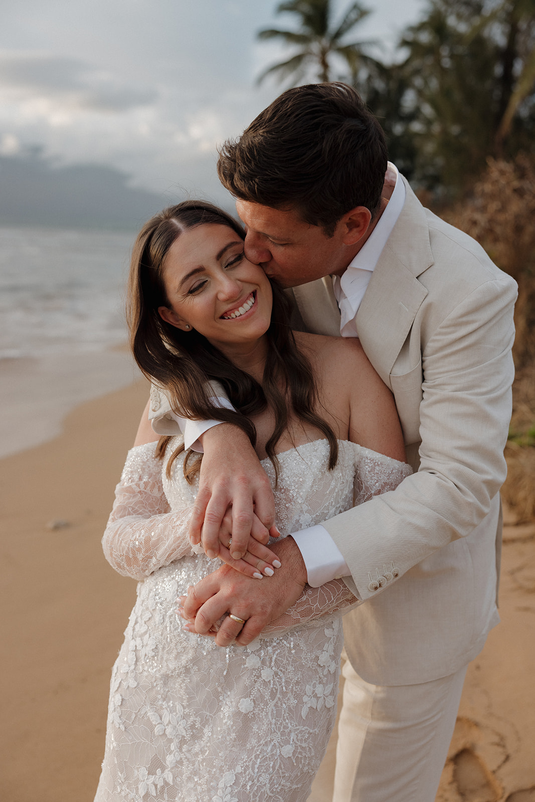 Groom kissing bride on the cheek while embracing her on the beach during their Maui elopement
