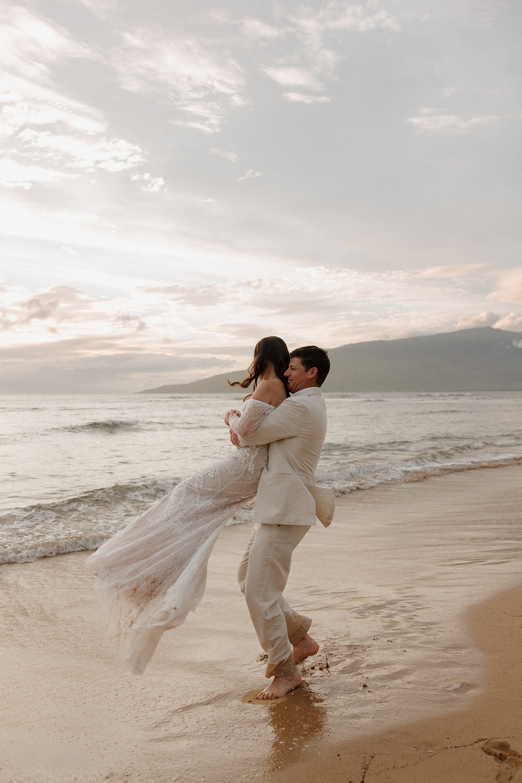 Groom lifting and spinning bride on the shoreline during their Maui elopement beach portraits

