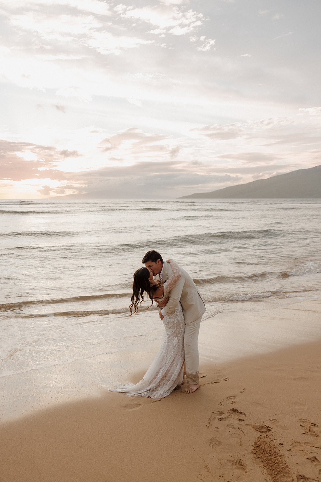 Groom dipping bride for a romantic kiss on the beach at sunset in Hawaii

