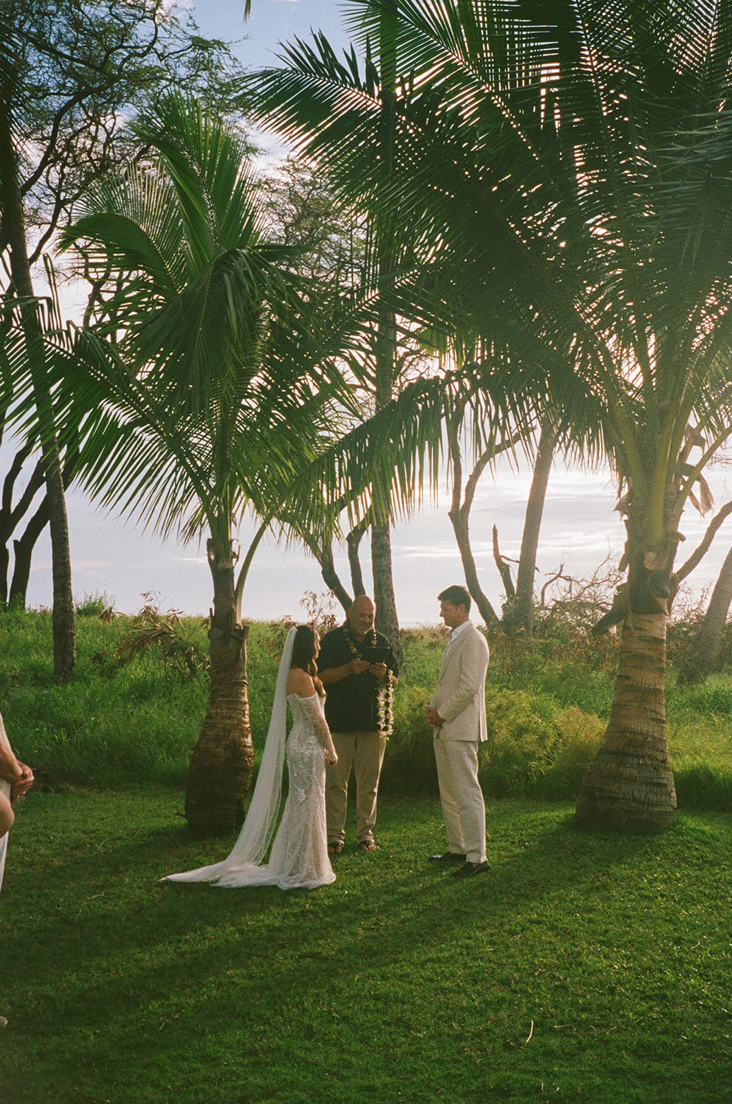 Bride and groom exchanging vows during their Maui elopement ceremony framed by palm trees and ocean light
