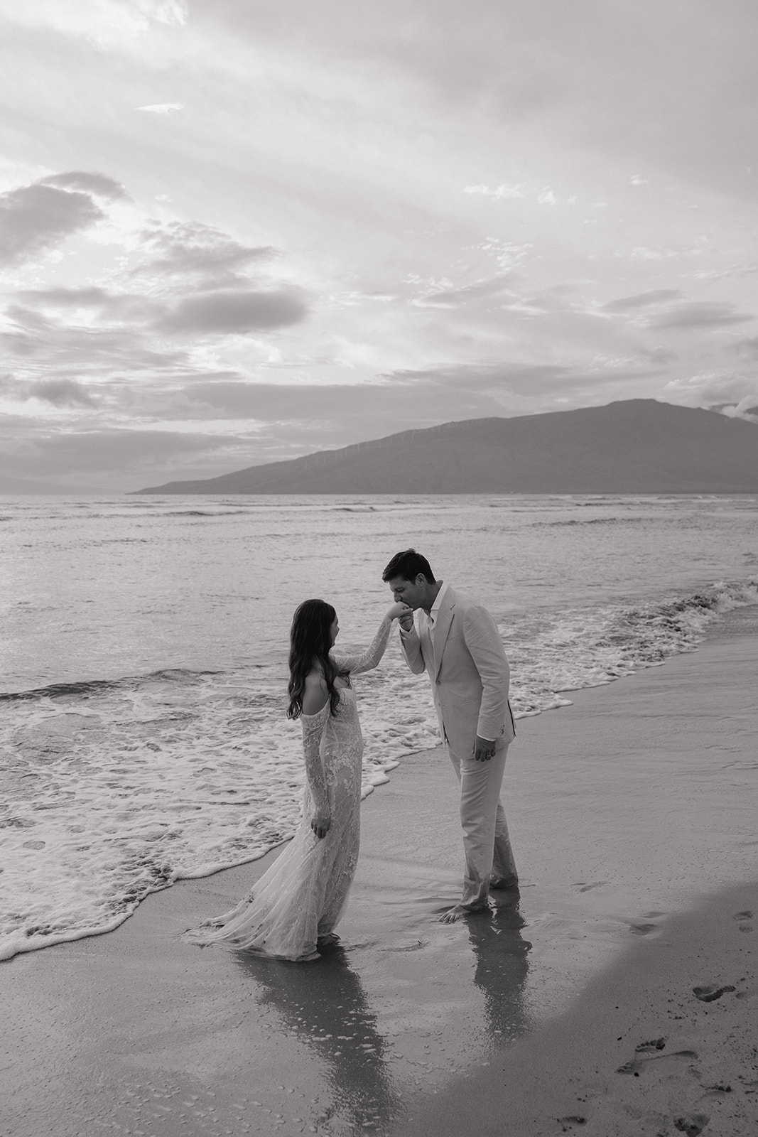 Black and white photo of groom kissing bride's hand on a Maui beach
