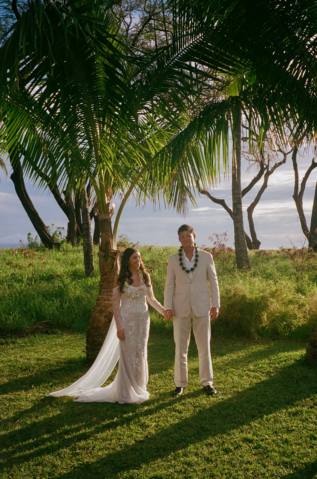 Bride and groom holding hands under a palm tree after their Hawaii wedding ceremony
