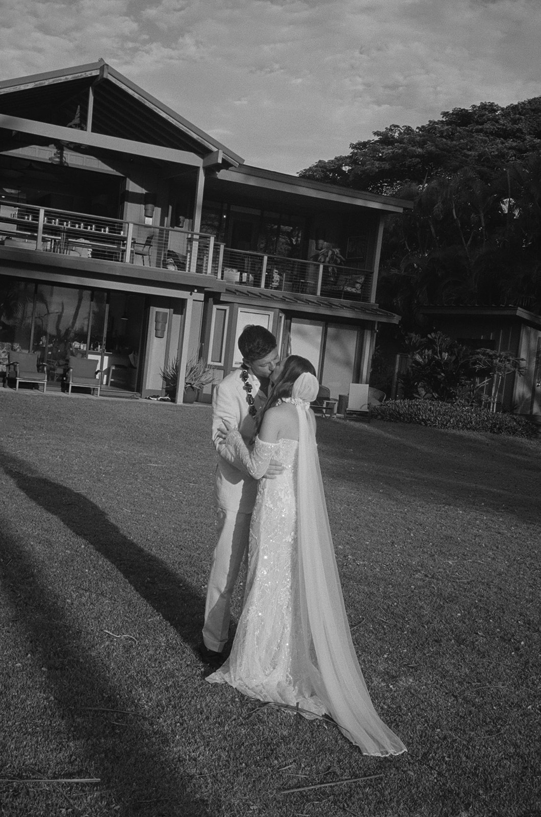 Black and white photo of bride and groom kissing on the lawn outside a Hawaii estate
