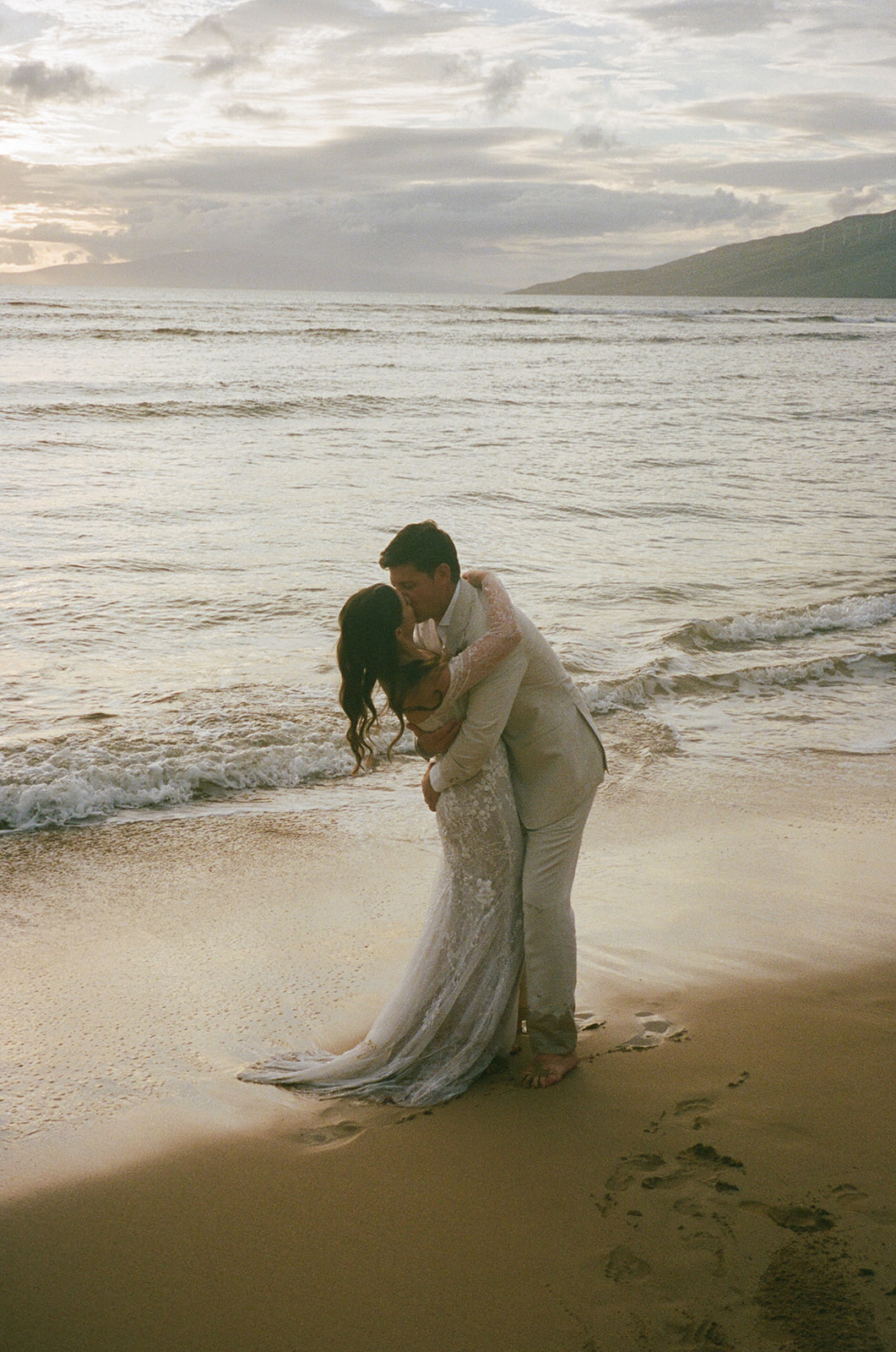 Groom dipping bride for a kiss on the beach at sunset in Hawaii
