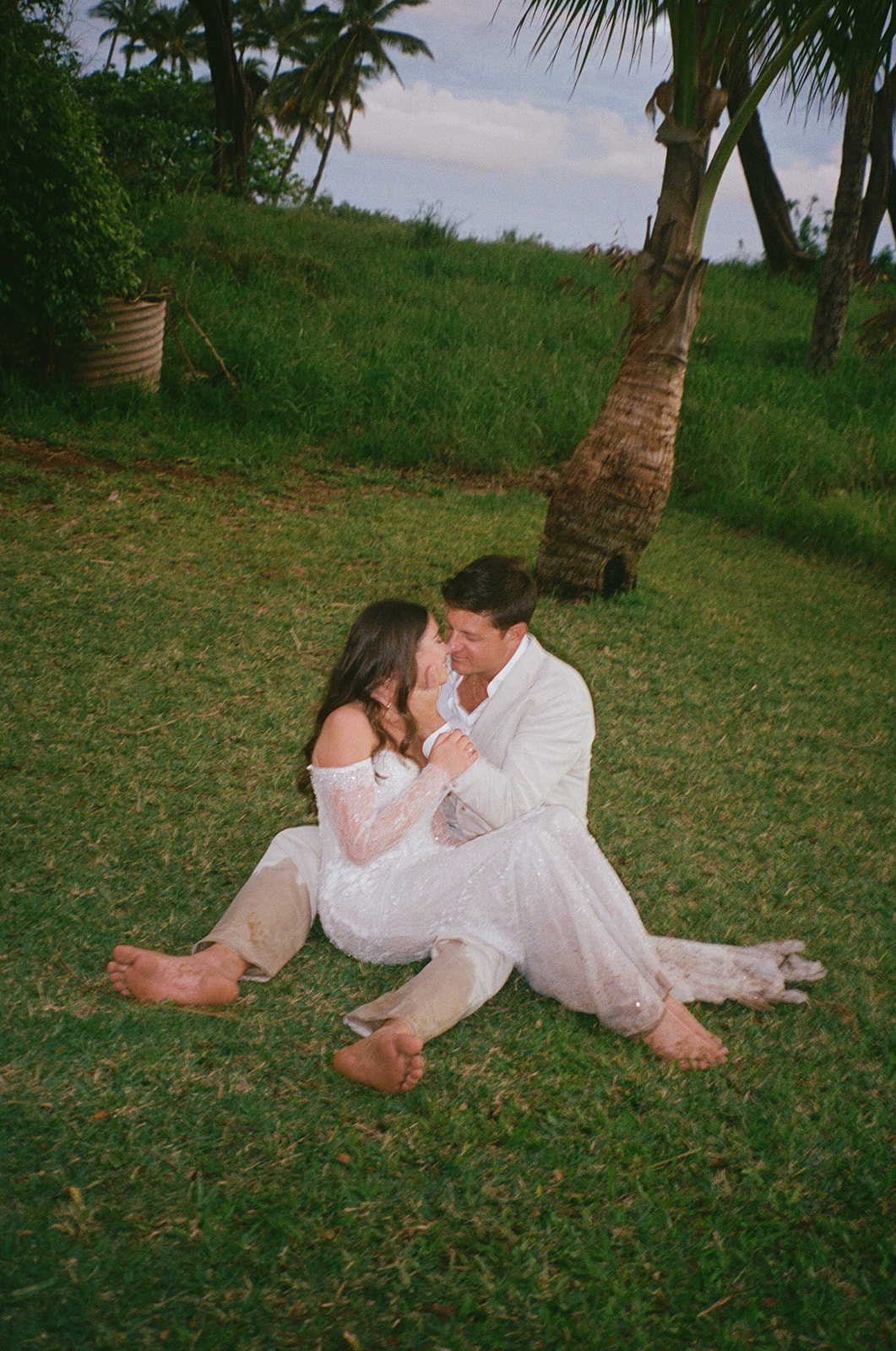 Bride and groom sitting barefoot together on the grass laughing during their Maui elopement
