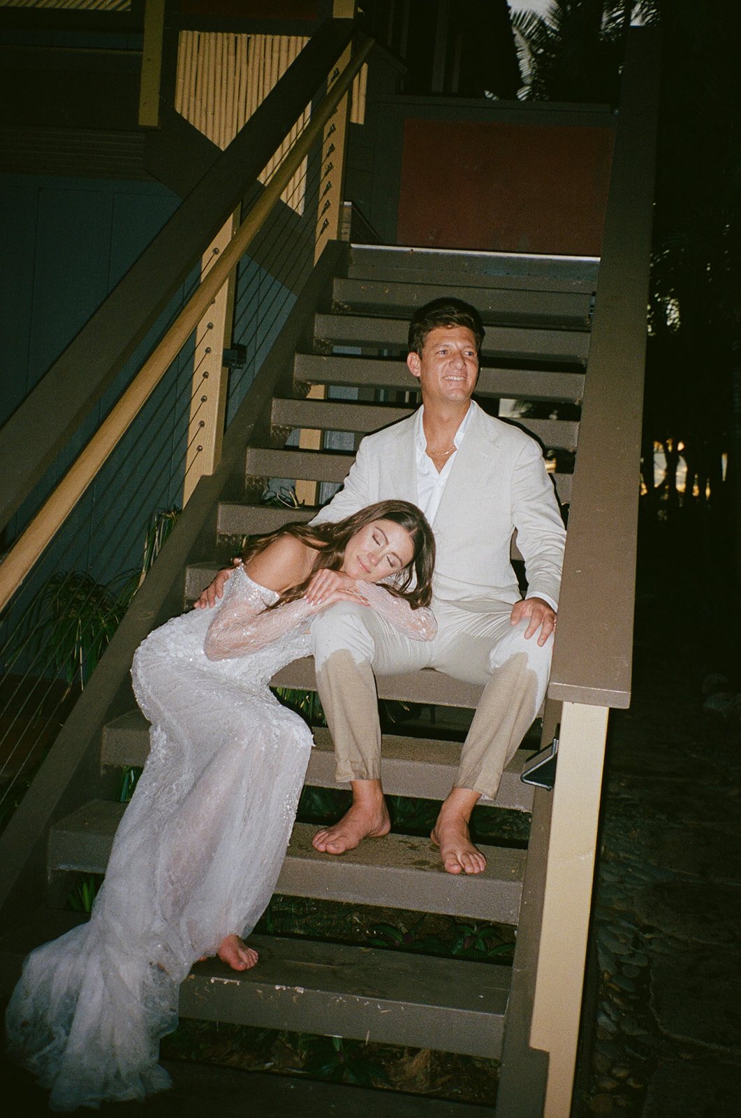 Bride resting her head on groom's knee while sitting barefoot on steps at a Hawaii wedding venue
