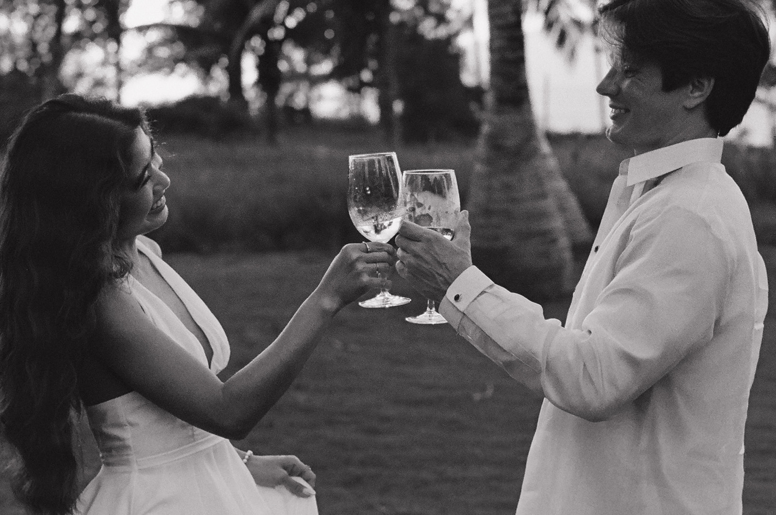 Black and white toast between bride and groom holding wine glasses at golden hour
