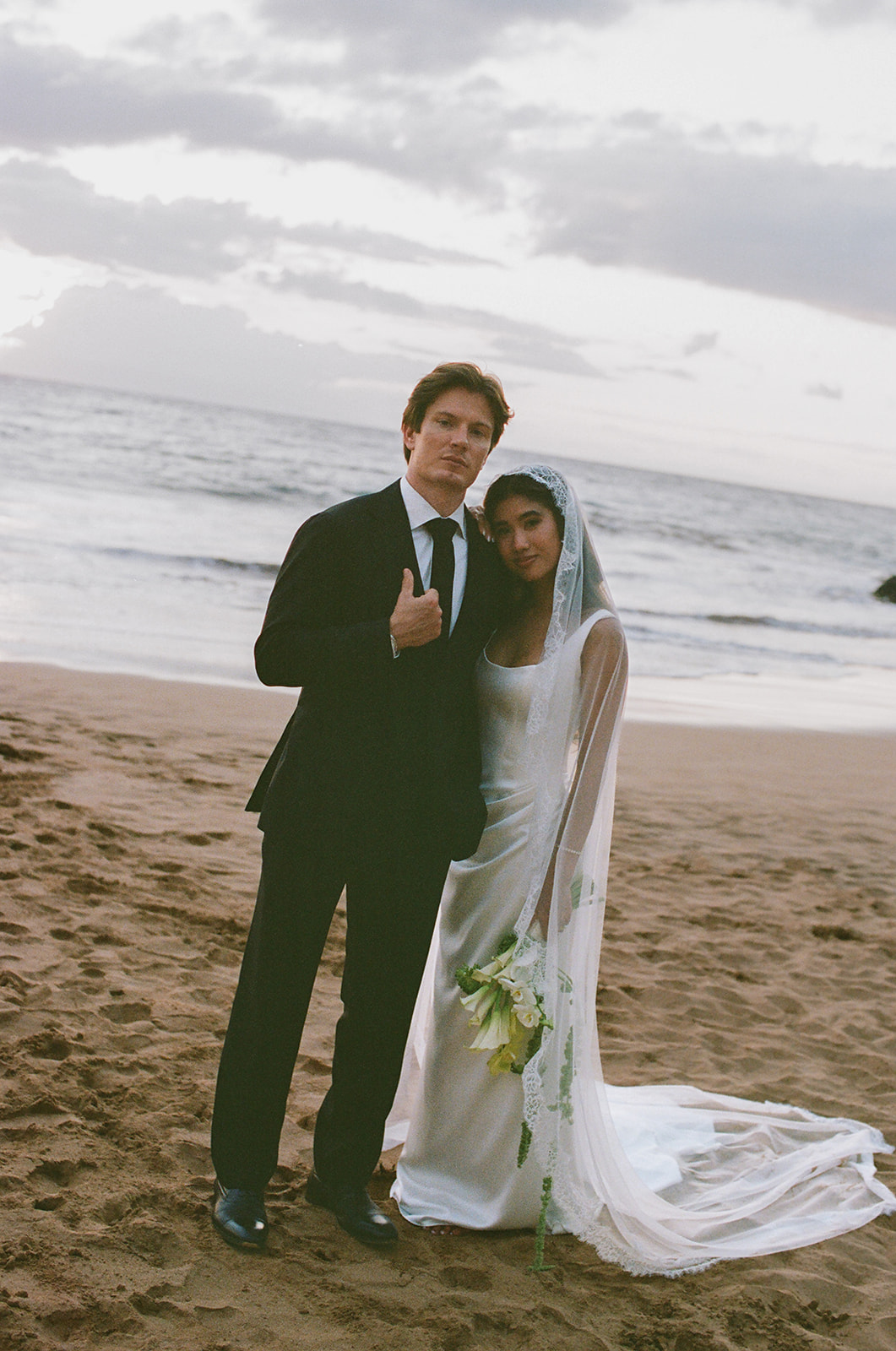 Wedding film photography portrait of the newlyweds standing together on the beach at sunset