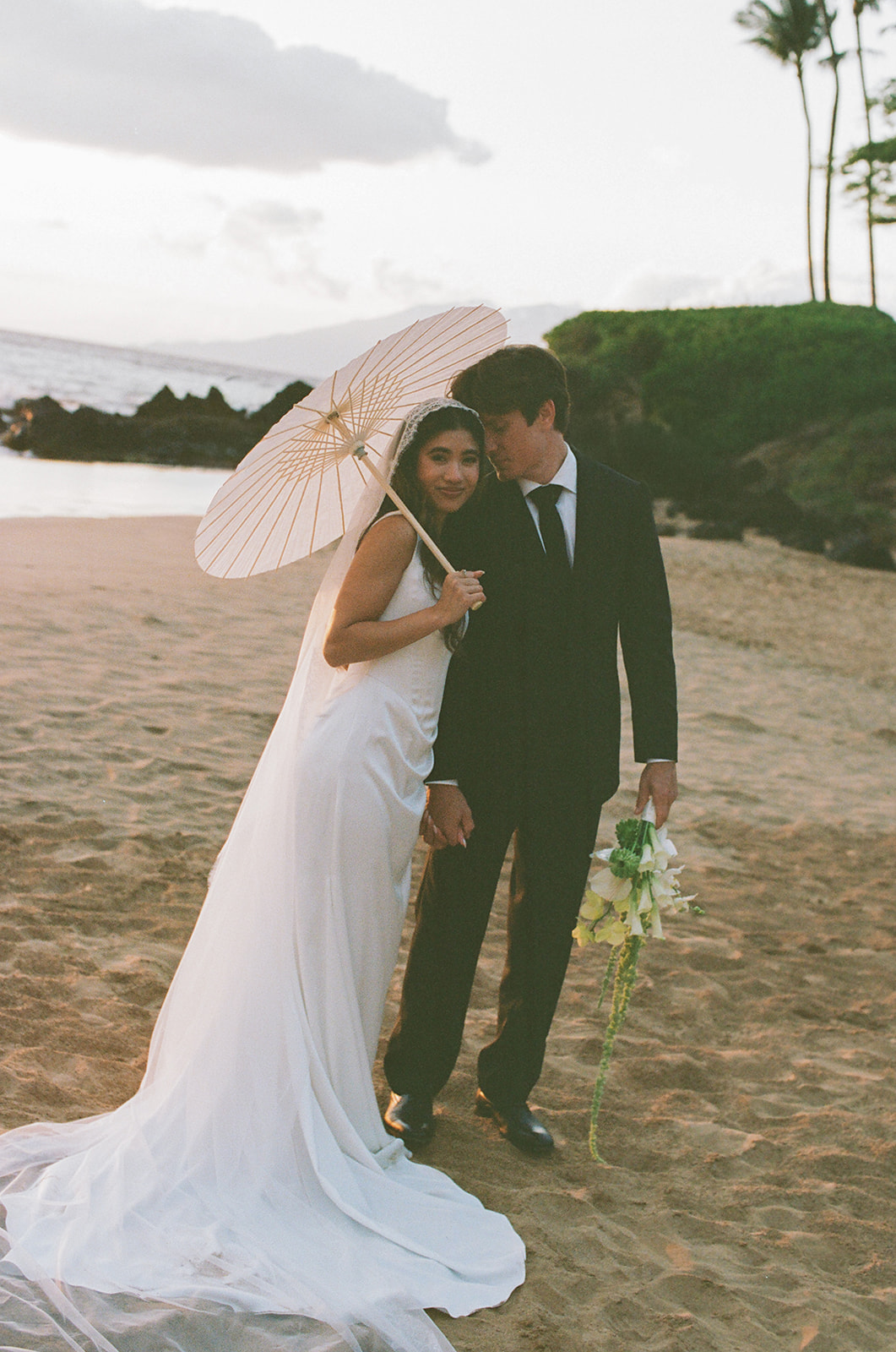 Wedding film photography of the couple sharing a quiet moment under a parasol on the beach
