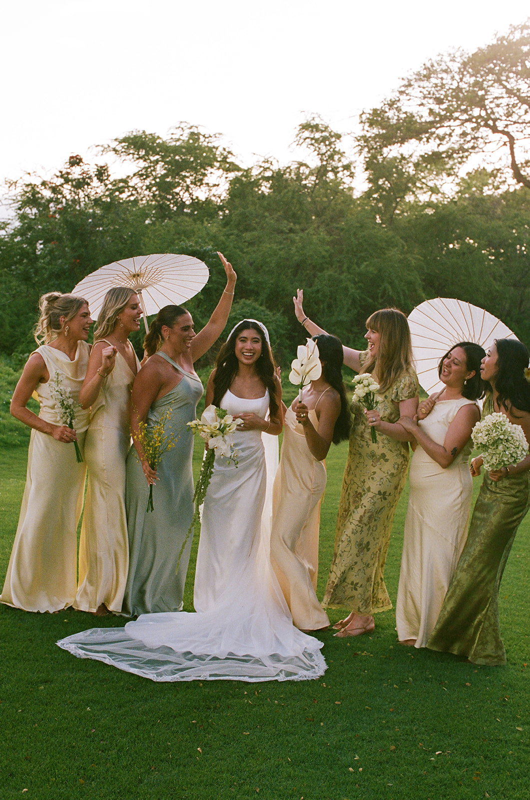 Wedding film photography of the bride and her bridesmaids cheering and laughing with parasols on the lawn
