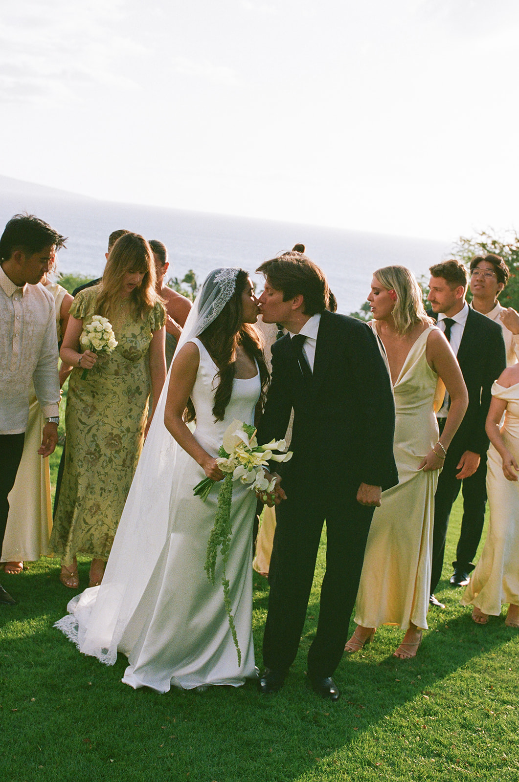 Wedding film photography candid of the bride and groom kissing surrounded by their wedding party
