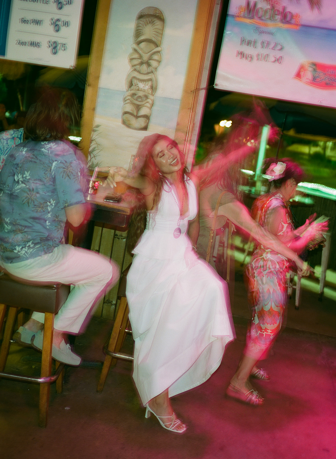 Bride dancing joyfully at a tiki bar with motion-blurred lights
