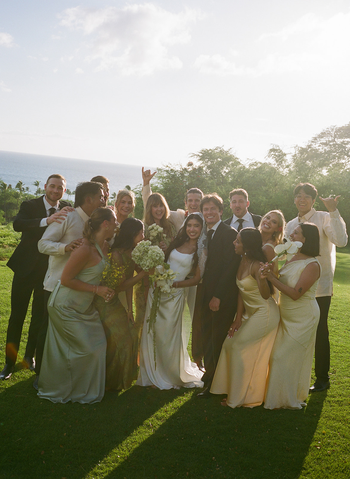 Wedding film photography group portrait of the bride, groom, and wedding party laughing together on the lawn
