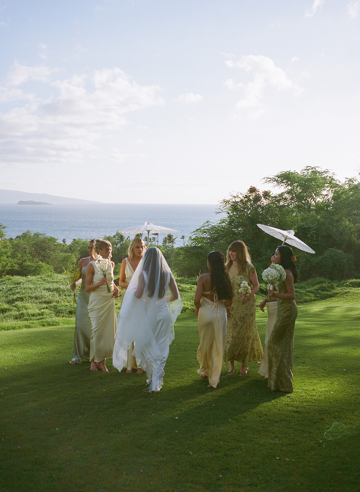 Wedding film photography of the bride walking with her bridesmaids across the lawn toward the ocean view
