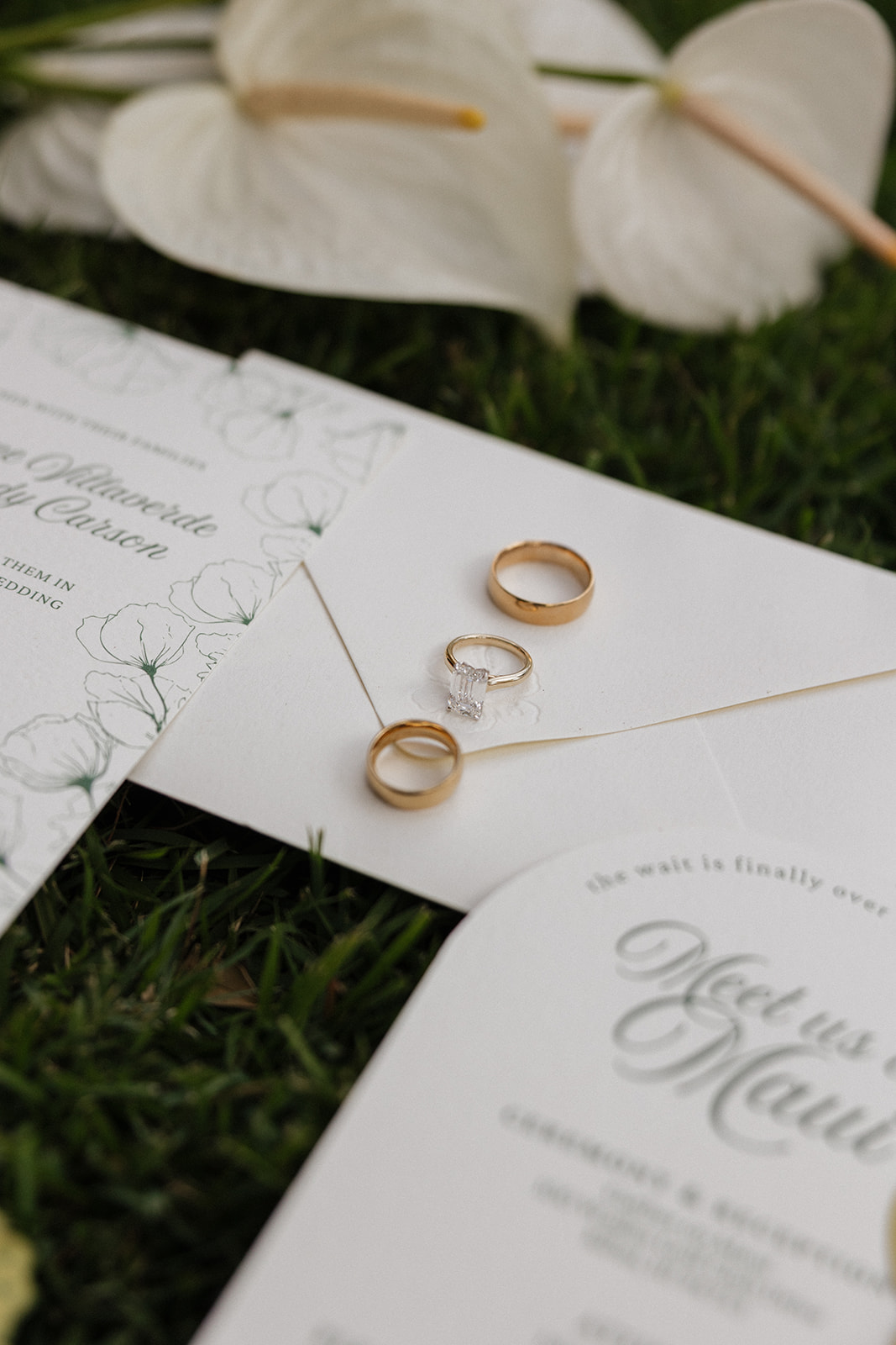 Wedding film photography flat lay of the wedding rings resting on the invitation envelope beside anthurium blooms
