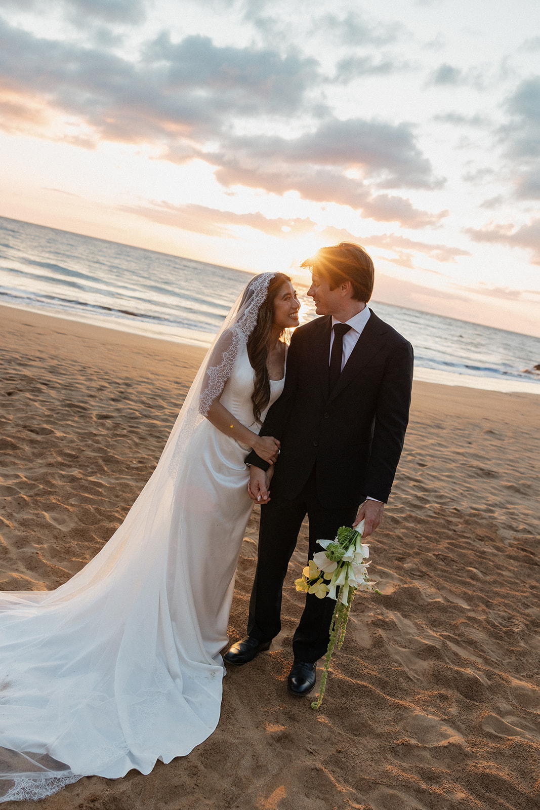 Bride and groom gazing at each other on the beach as the sun sets behind them
