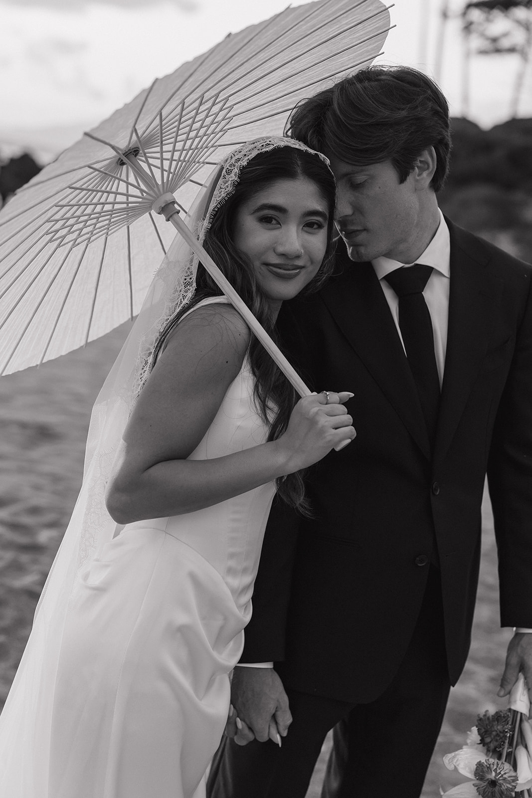 Wedding film photography black and white portrait of the bride and groom under a parasol on the beach
