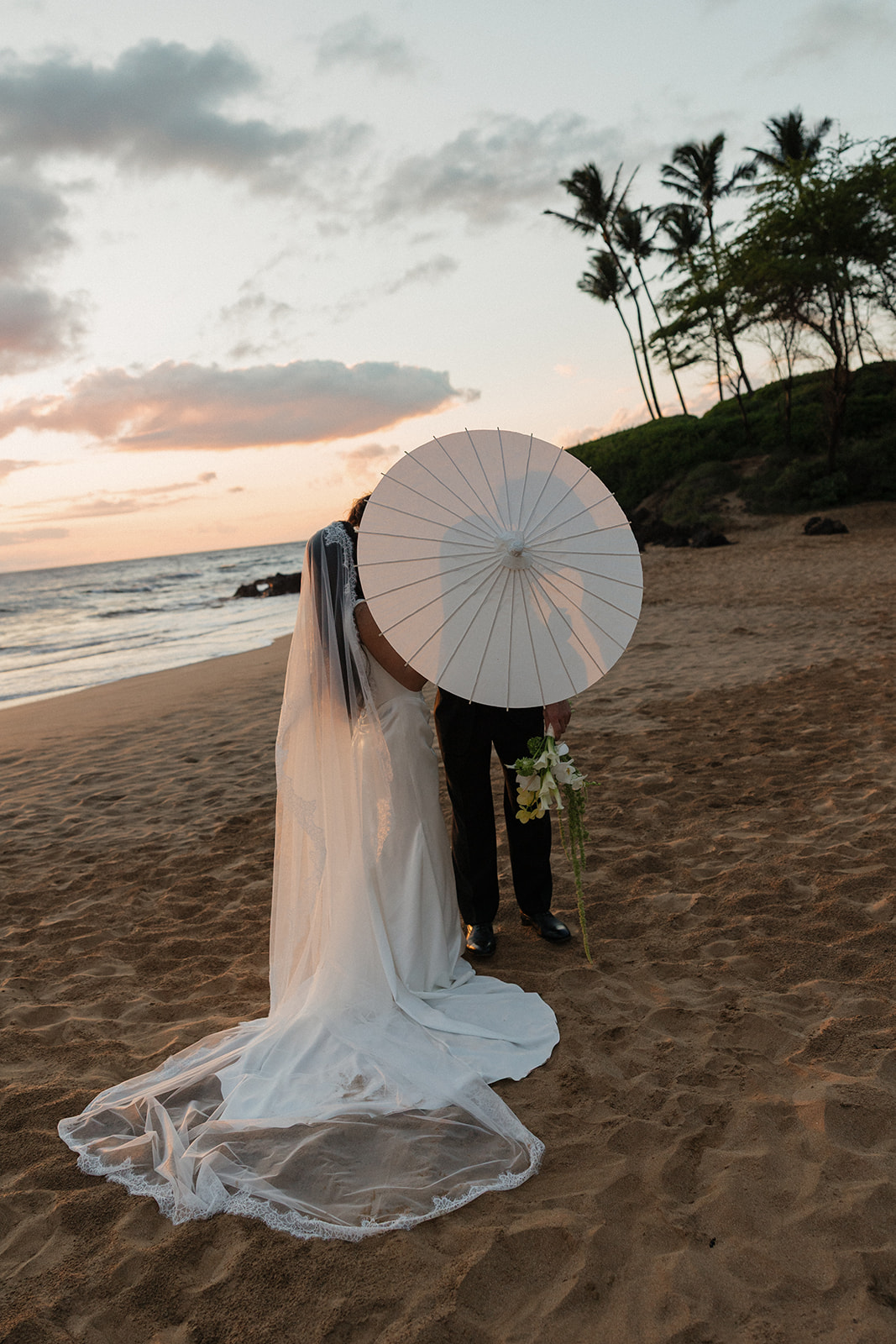 Wedding film photography of the bride and groom sheltering under a parasol on the beach at dusk