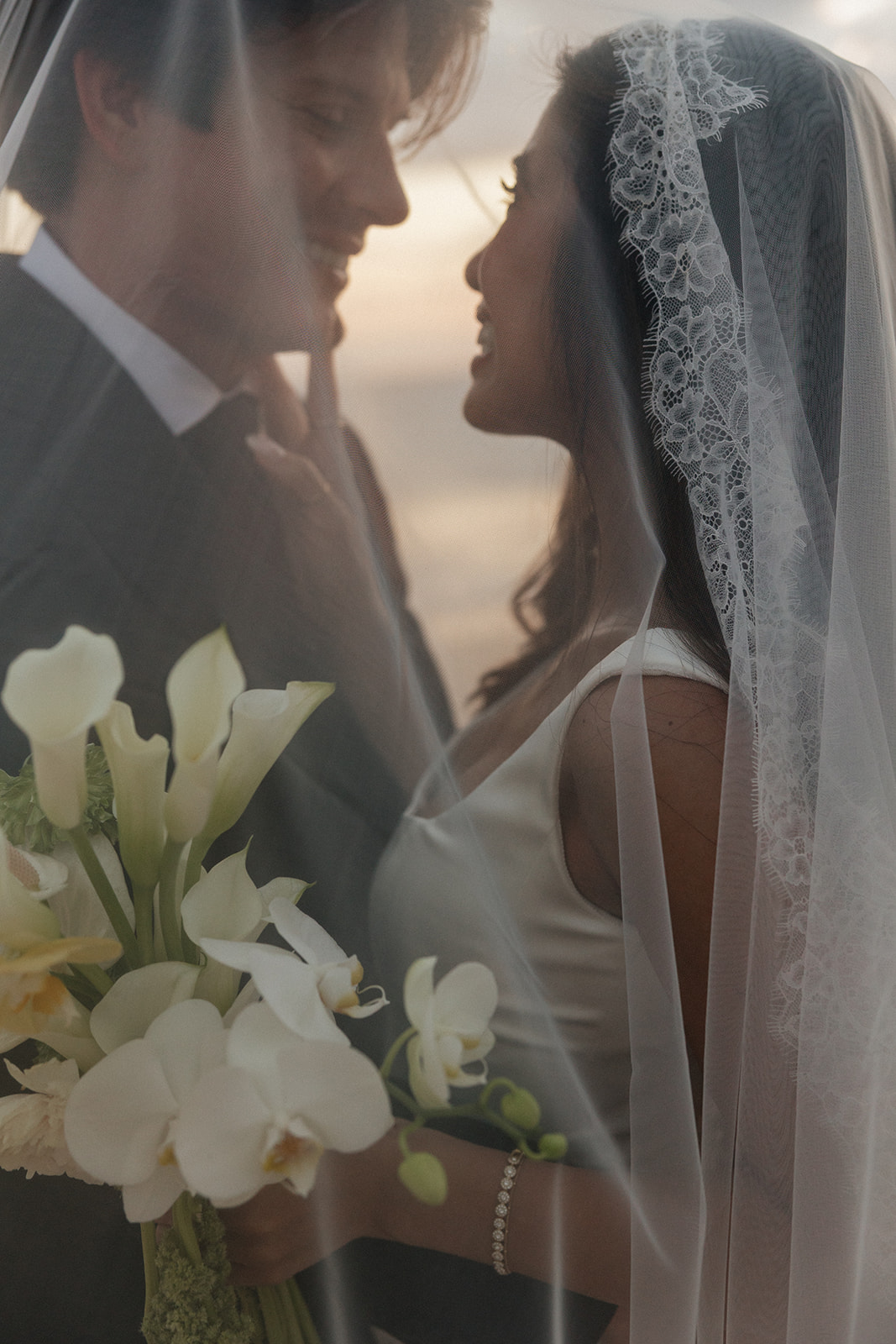 Wedding film photography of the bride and groom gazing at each other through her sheer veil, bouquet in frame
