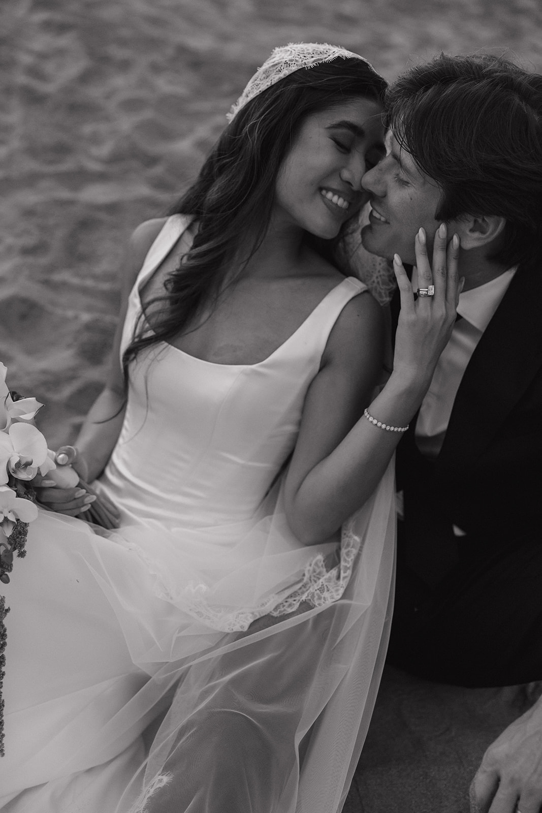 Black and white close-up of the bride and groom embracing cheek to cheek on the sand
