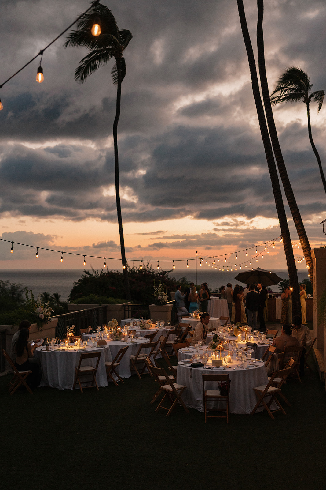 Wedding film photography of the oceanfront reception space glowing at dusk with string lights and table settings
