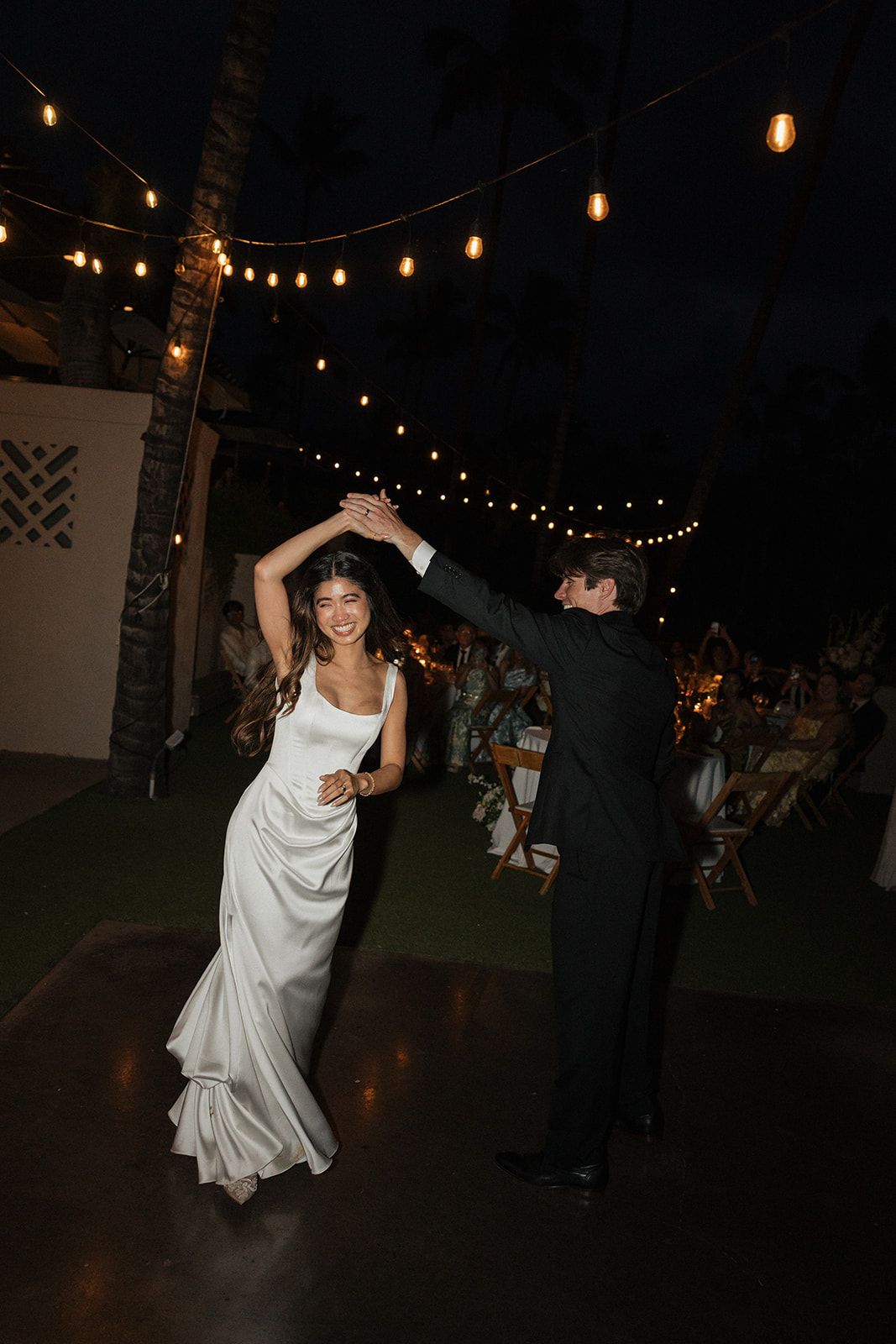 Bride and groom dancing together under string lights at their reception
