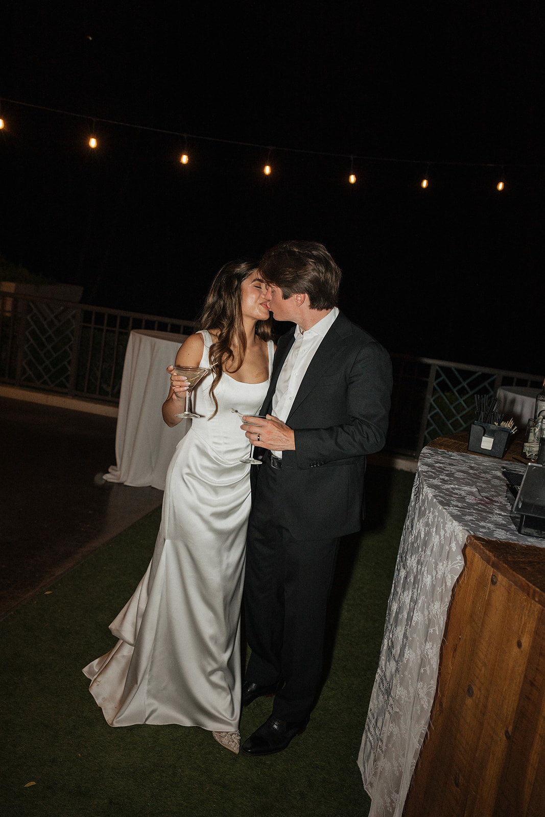 Wedding film photography of the bride and groom sharing a kiss while holding martinis at the bar

