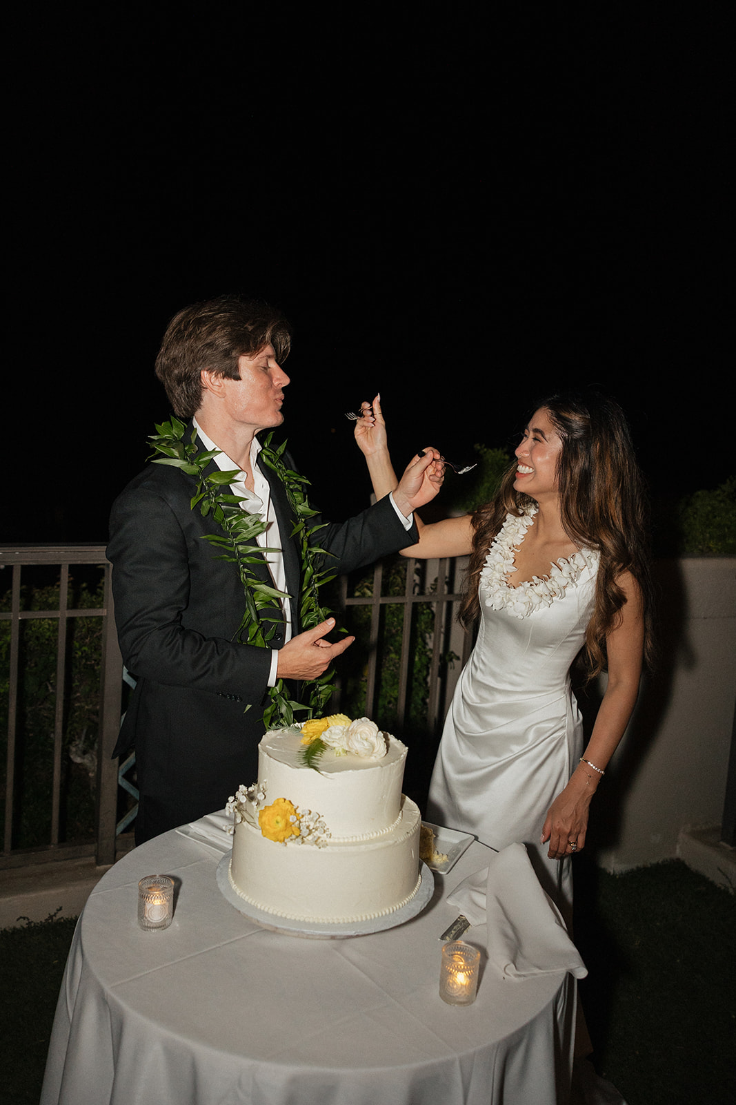 Bride and groom feeding each other cake during their reception at night
