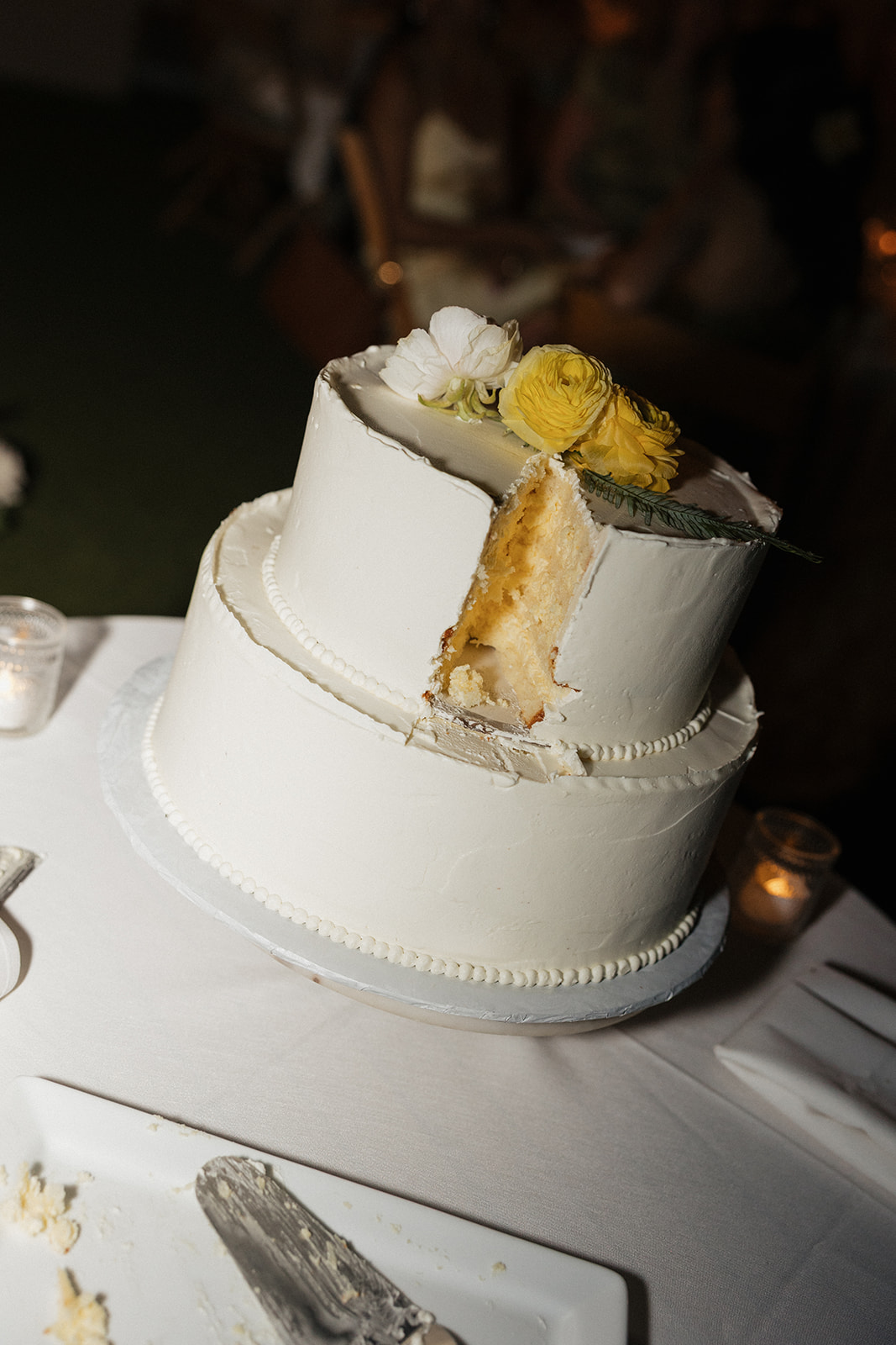 Wedding film photography close-up of a two-tier cake with yellow and white florals, sliced into
