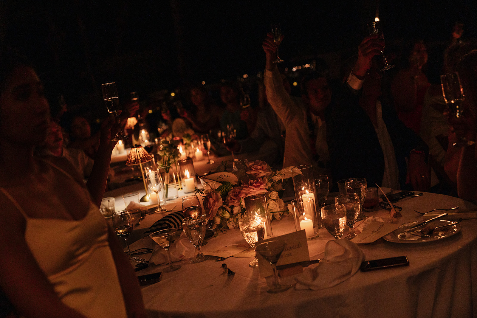 Wedding film photography of guests raising their glasses in a candlelit reception toast
