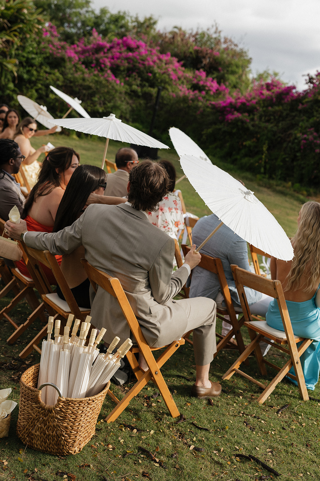 Wedding guests holding white parasols to shade themselves during the outdoor ceremony
