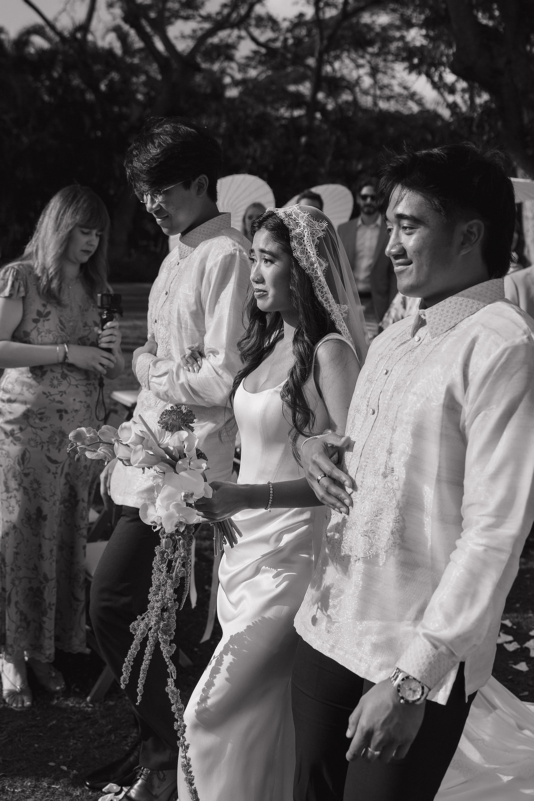 Wedding film photography black and white candid of the bride walking down the aisle with her brothers.
