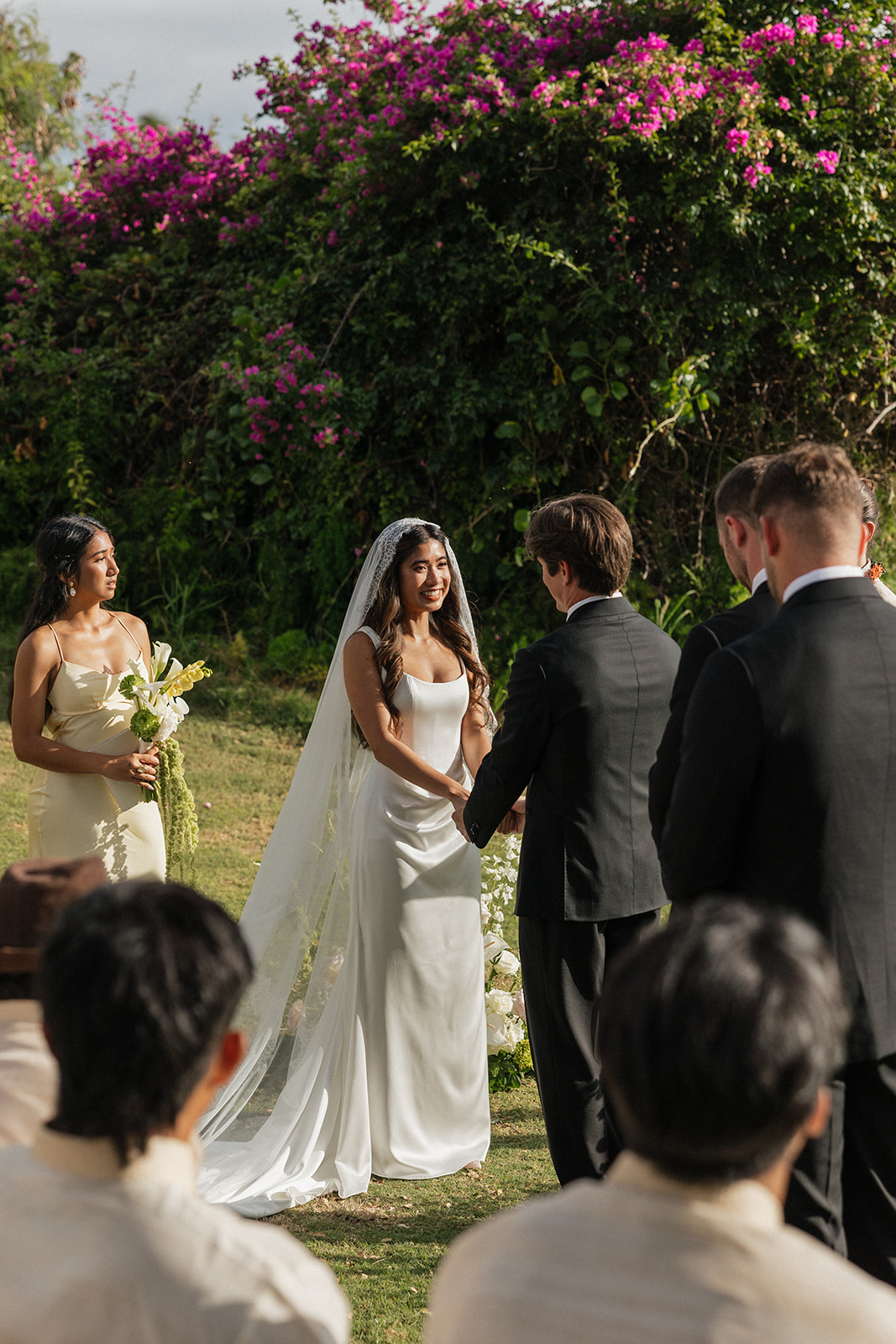 Bride and groom holding hands at the altar in front of blooming bougainvillea
