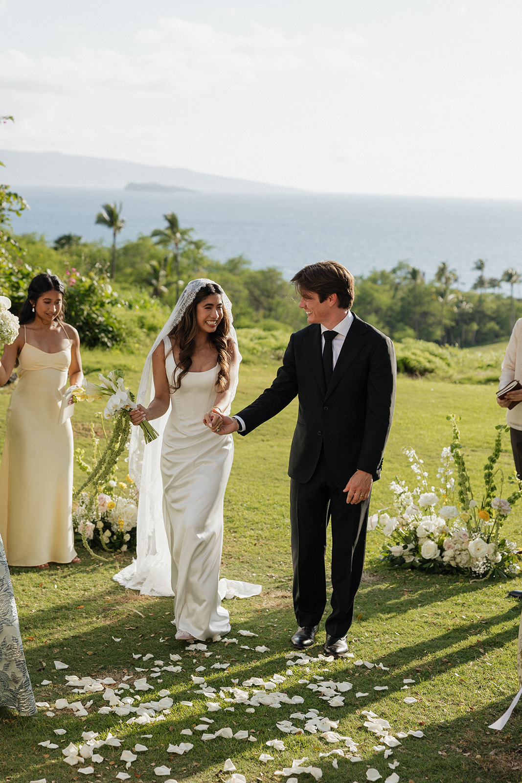 Bride and groom smiling at each other while walking down the petal-strewn aisle
