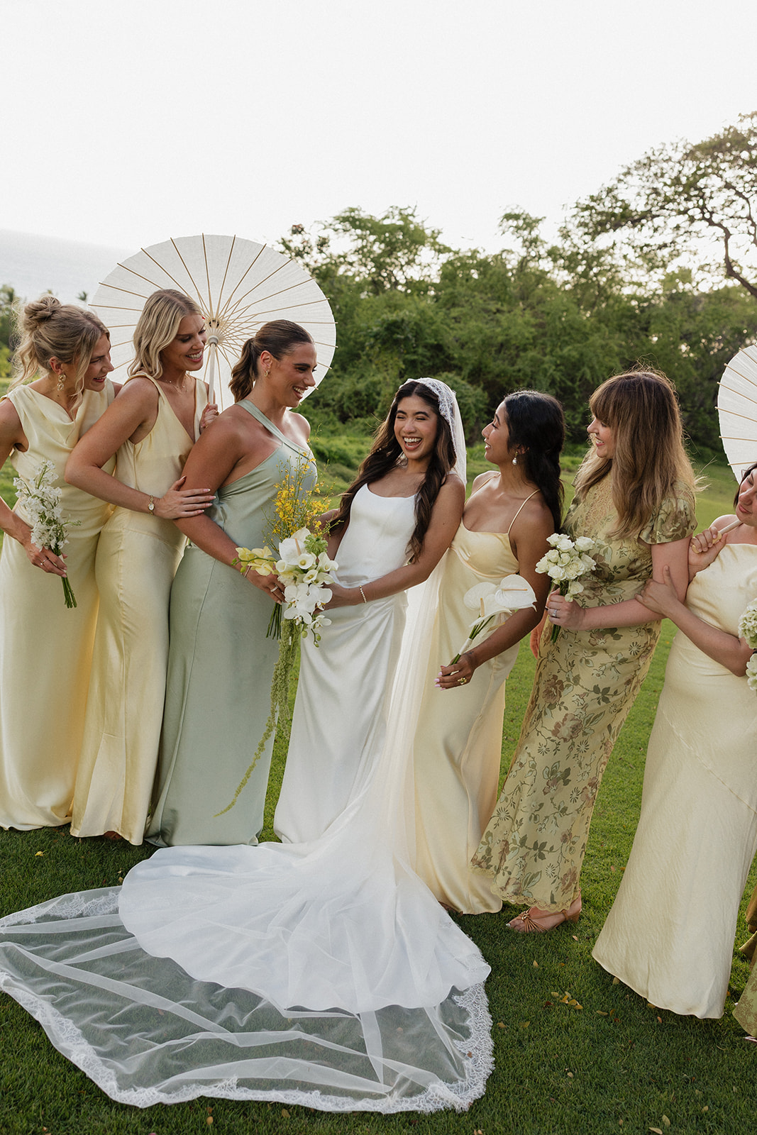 Wedding film photography of bridesmaids gathered around the bride, laughing under a parasol
