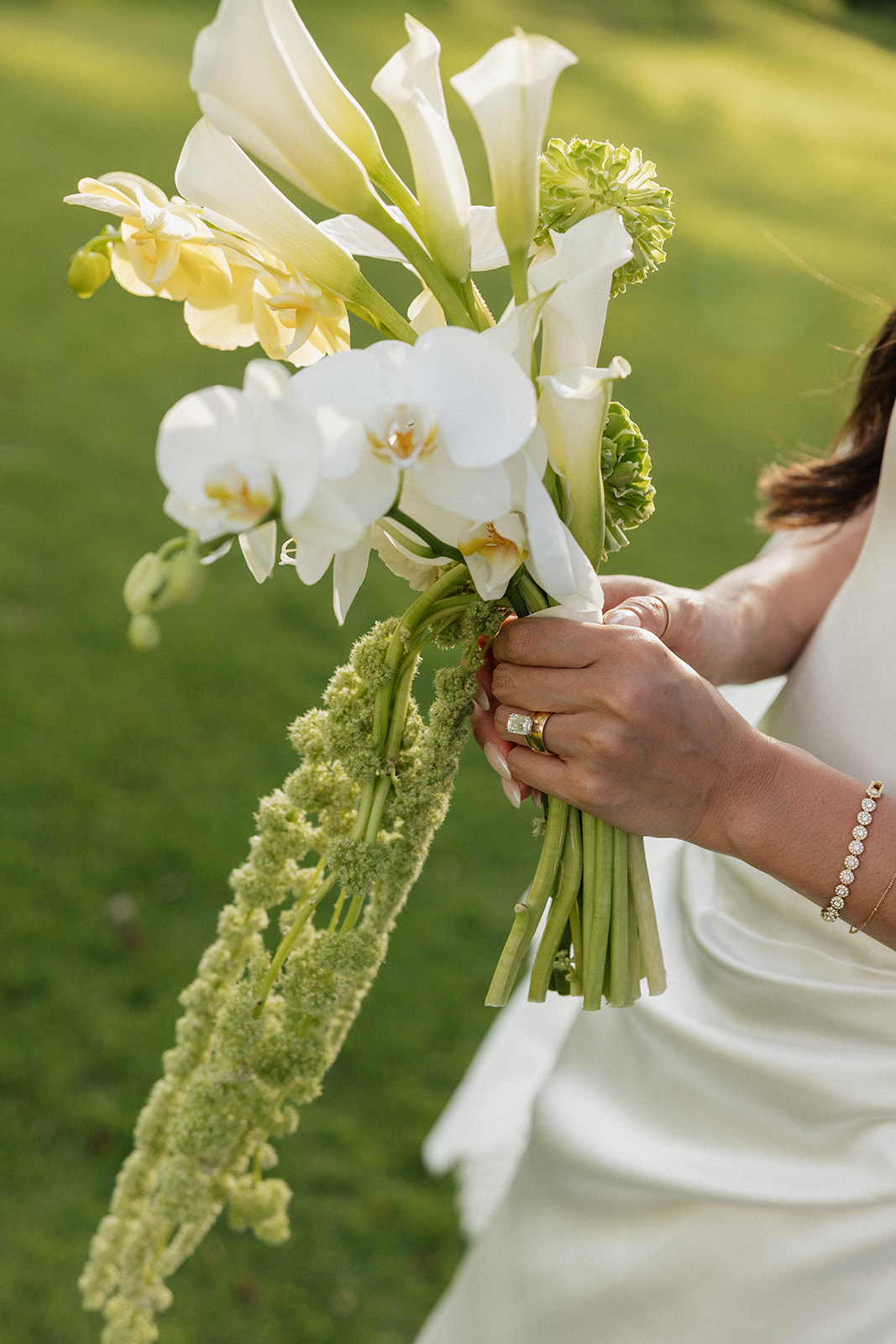 Close-up of the bridal bouquet of calla lilies, orchids, and trailing amaranthus held in the bride's hands
