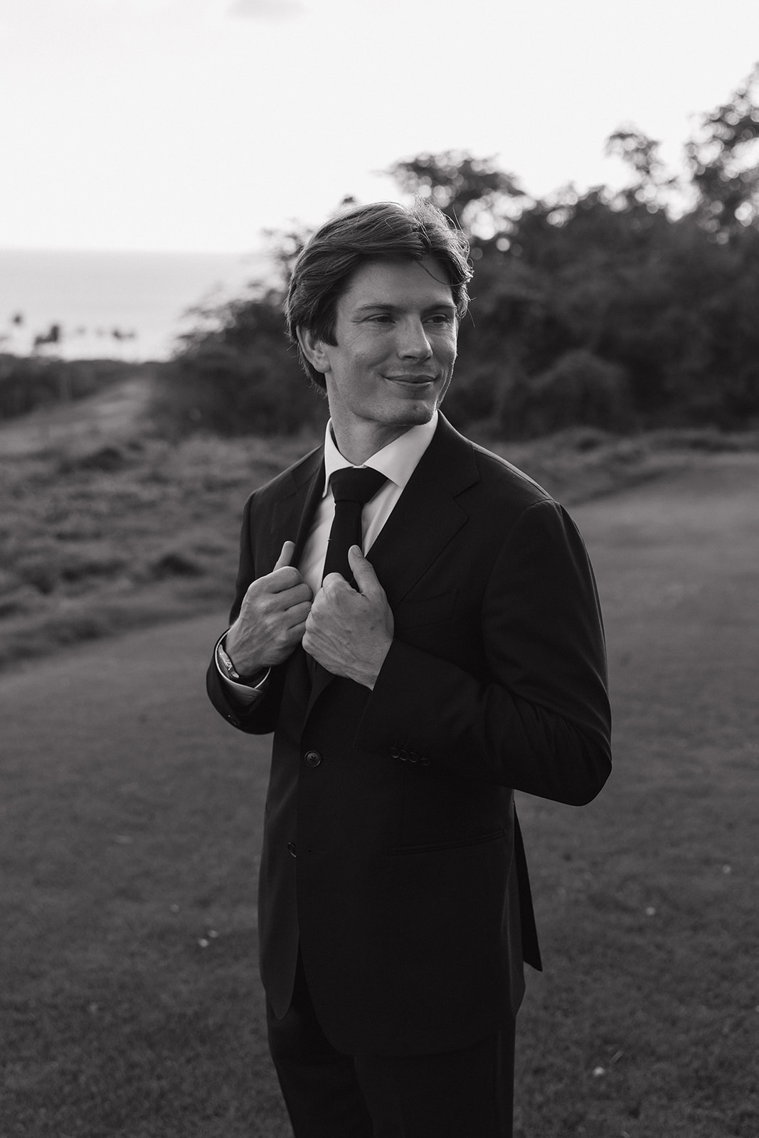 Wedding film photography black and white portrait of the groom adjusting his jacket lapels
