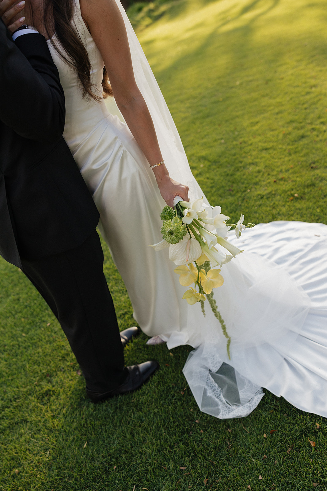 Bride and groom holding hands, her bouquet trailing amaranthus over her satin gown
