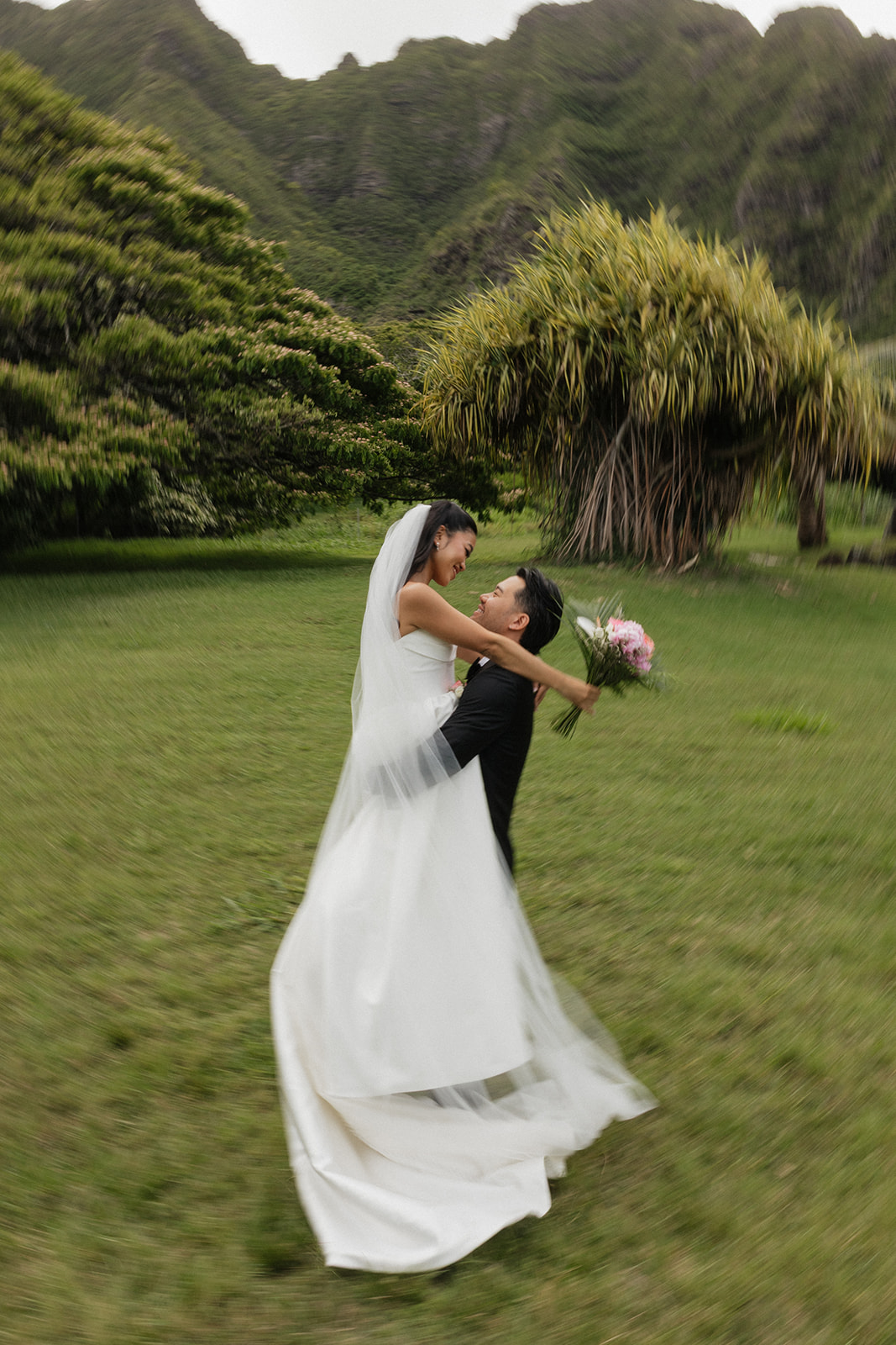 Groom spinning bride in his arms during a joyful rain-soaked couples portrait at their Kualoa Ranch Wedding, with motion blur capturing the energy of the moment