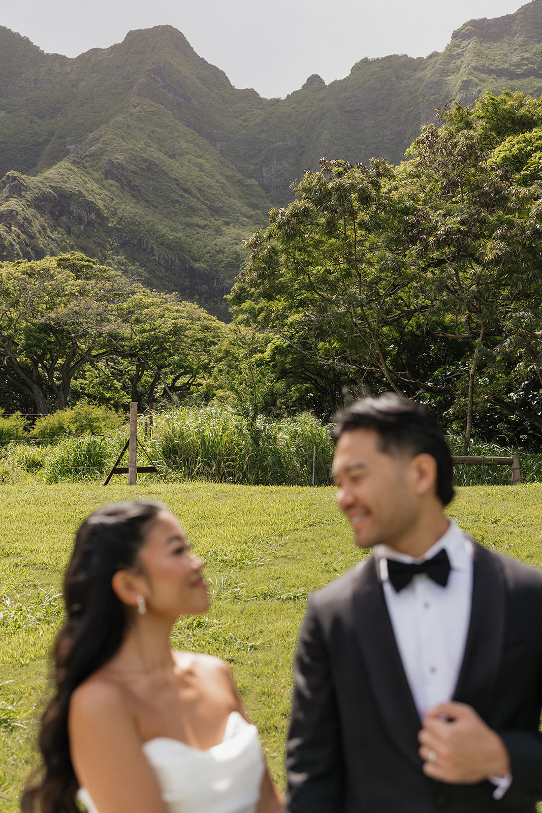 Candid portrait of bride and groom laughing together at their Kualoa Ranch Wedding, both slightly out of focus with the vivid green Ko'olau mountains sharp in the background