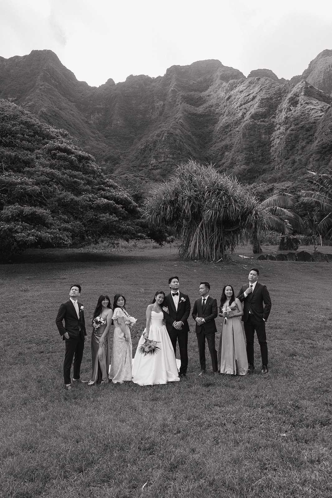 Black and white editorial-style wedding party portrait at Kualoa Ranch Wedding, with the entire bridal party posed casually in front of the rugged Ko'olau mountain range