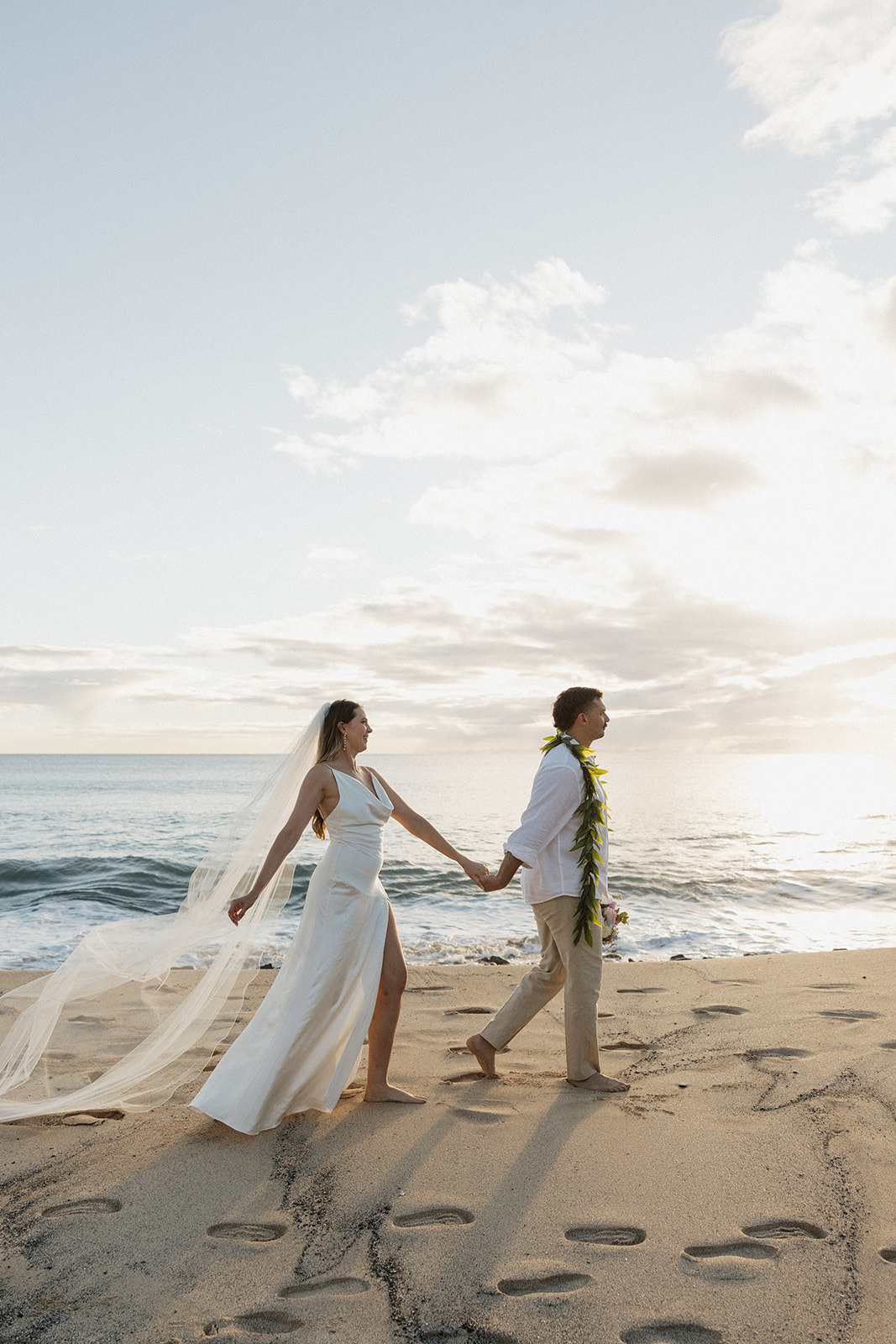 Bride leading her groom by the hand down the beach, veil blowing in the wind.